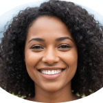A smiling woman with curly hair looks directly at the camera in a close-up portrait against a plain background.